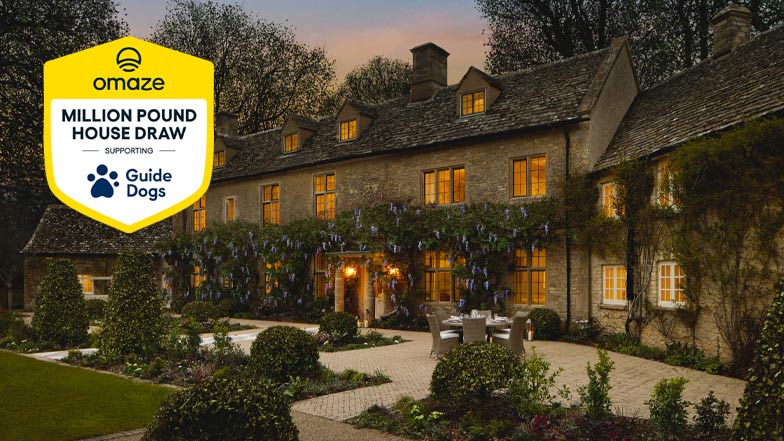 The house you can win in the Omaze Cotswolds House Draw, lit up in the evening and with the Omaze shield logo on the left