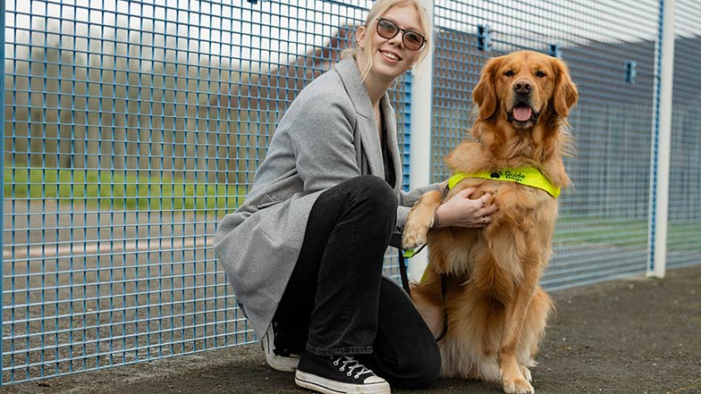 Hannah crouches down beside her golden retriever guide dog