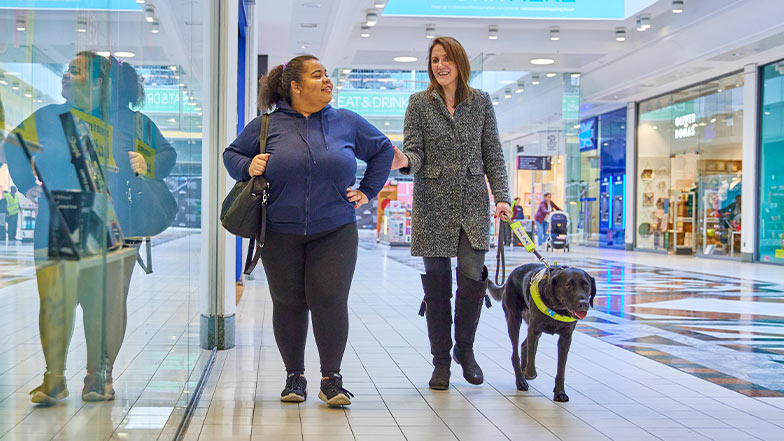 A guide dog owner being guided through a shopping centre