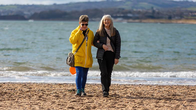 a person with sight loss and their sighted guide on a beach