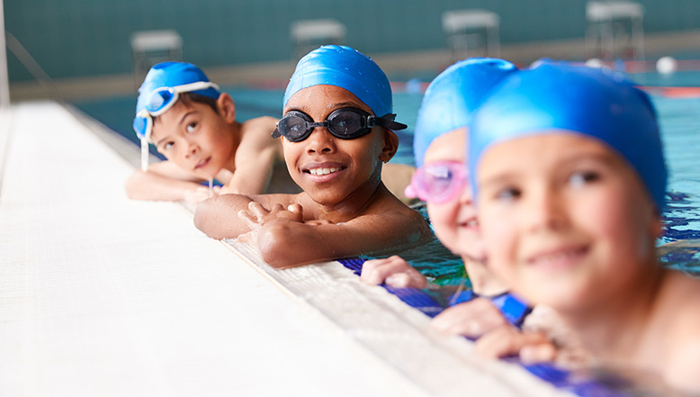 Group of children smiling in a swimming pool wearing swimming hats