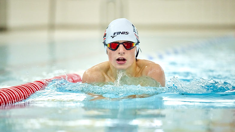 Archie swims toward the camera. He is wearing a swimming cap and goggles.