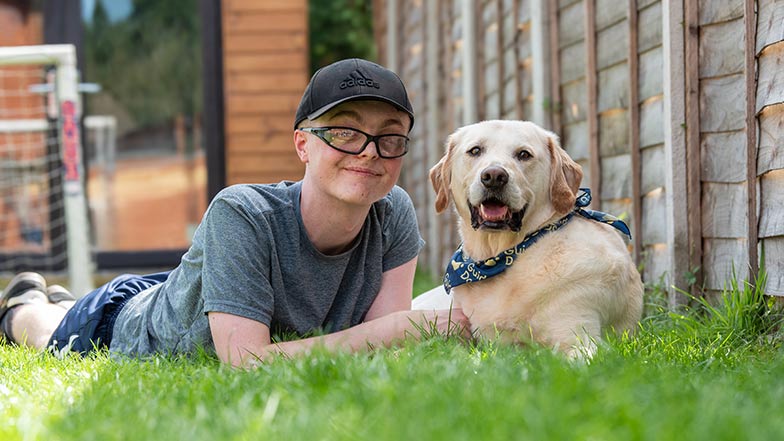 Declan, a young service user, and his buddy dog, lie on the grass in their garden.