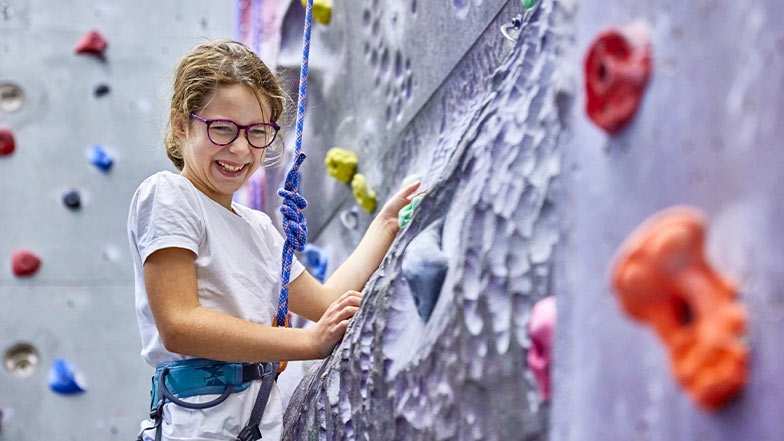 Nine-year-old Erin laughs and smiles as she plays on a climbing wall.