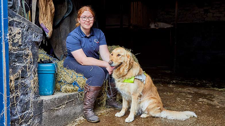 Ella and guide dog Katie sitting together in a barn