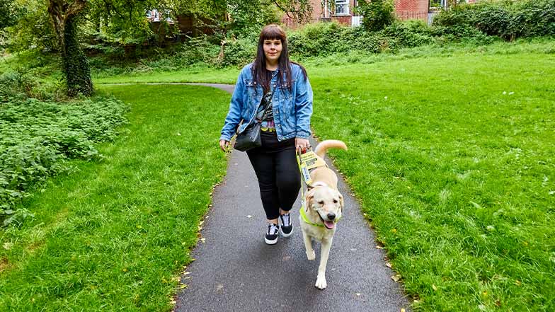 Lorna walks towards camera, being guided by her guide dog, Yarren.