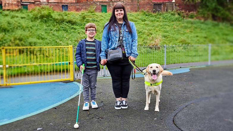 Lorna, her guide dog Yarren, and her son Rex, stand in a park.