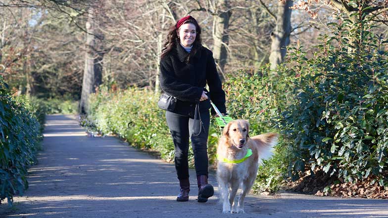 Taylor and her guide dog walk along a sunny path together.