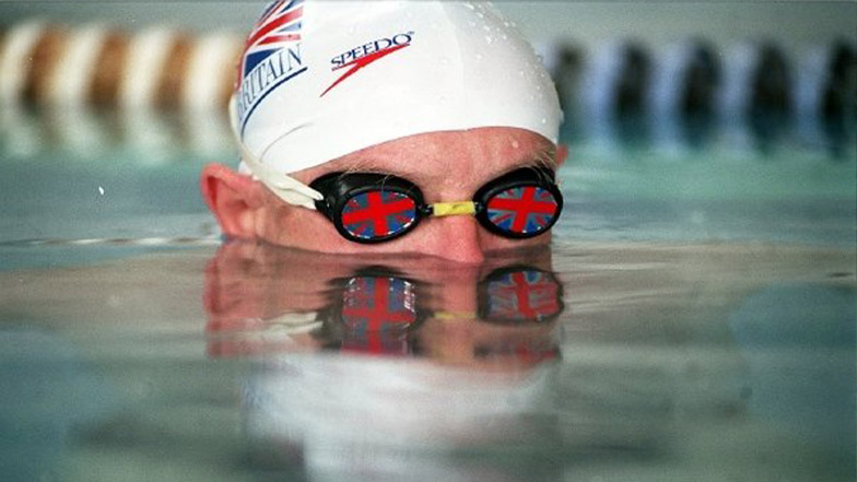 Tim swims in a pool wearing goggles and a swimming cap.