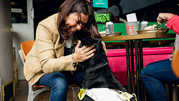 A smiling guide dog owner with her guide dog sitting in a café 
