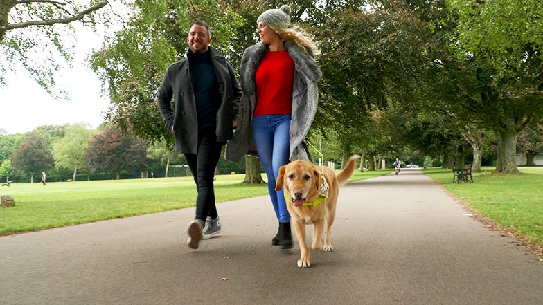 Guide dog owner Stacey walking in a park with guide dog and a man 