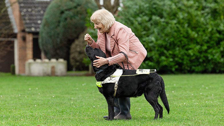 Guide dog owner Danni holding a treat for guide dog Joker outside on the grass.