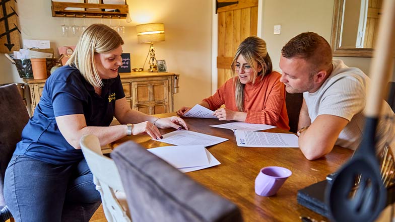 A Habilitation Specialist sits at a dining table with the parents of young service user, Margot.
