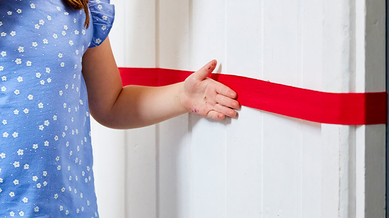 A little girl traces a ribbon with her hand to navigate a school corridor.