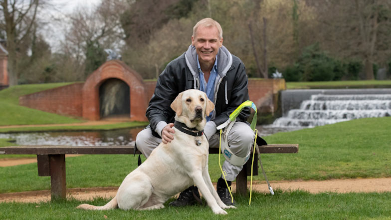 Paul sitting with guide dog Bolt on a bench alongside a waterway