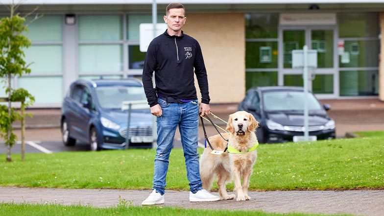 Scott and guide dog Milo stood outside of a university building.