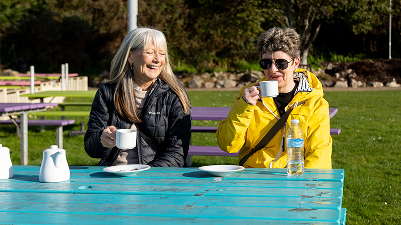 Suzanne has coffee with volunteer sighted guide Jan, the pair are laughing and happy
