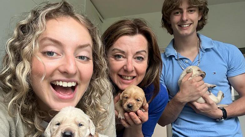 Caroline and her family smile to the camera while holding puppies.