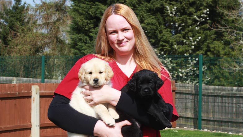 Dr Helen smiles to the camera, holding two guide dog puppies.