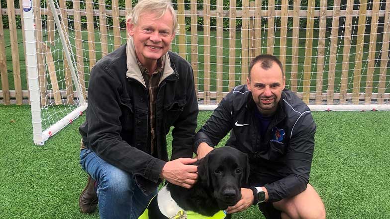 Martin and guide dog owner Craig kneel on a football pitch with guide dog Comet.