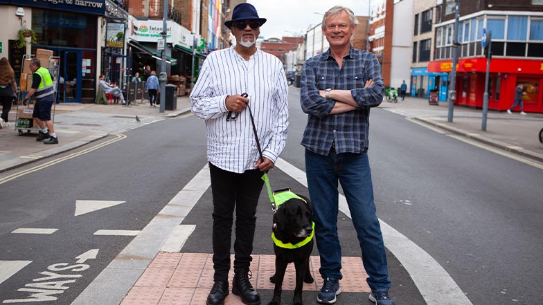 Martin and David stand in a high-street with Scooby, David's guide dog