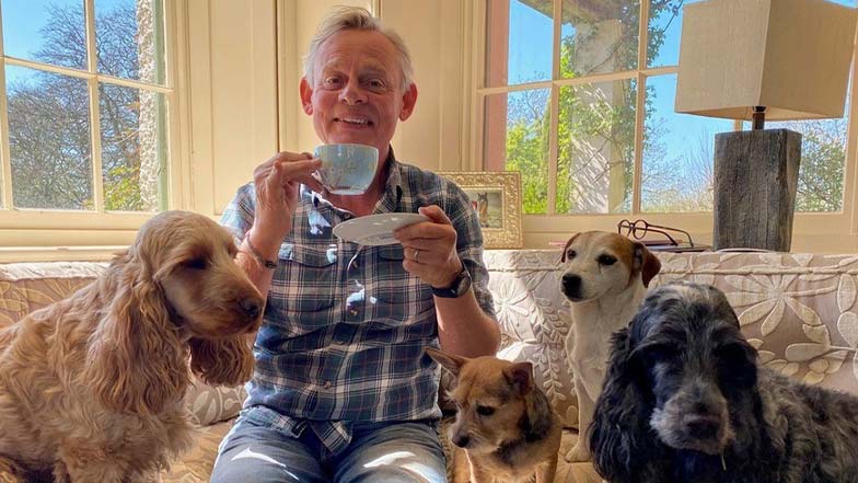 Martin with his other dogs in his home. He is smiling and holding a tea cup.