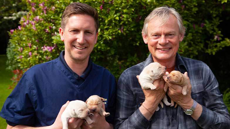 Martin and Tim smile to camera, each holding two newborn puppies.