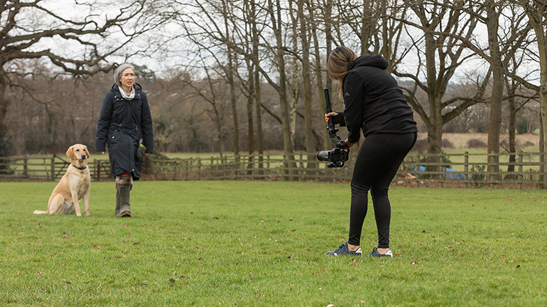 A Video Producer filming a rehomer and rehomed guide dog in an open field