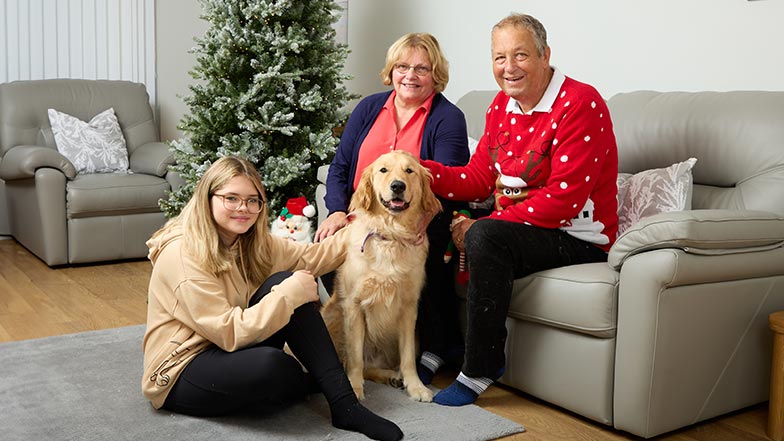 Tony wearing a Christmas jumper, sitting with his family and Angus in their living room.