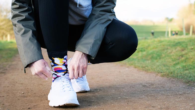 A person bending down tying up their shoe laces with Walk Your Socks Off socks