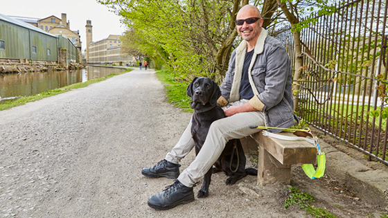 Terry sitting on a bench with guide dog, Spencer, sat between his legs