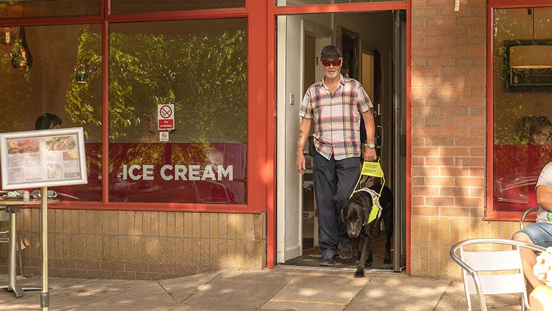 A guide dog owner leaves a café with his guide dog.