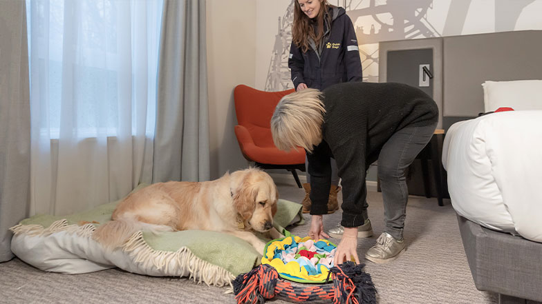 A guide dog owner and Guide Dog Mobility Specialist prepare an enrichment toy for a guide dog.