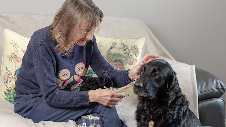 A guide dog owner pets her retired guide dog, as they sit in the living room.