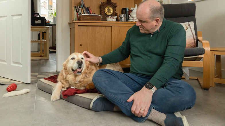 Retired guide dog, Benji, sits on the floor beside his owner, John.
