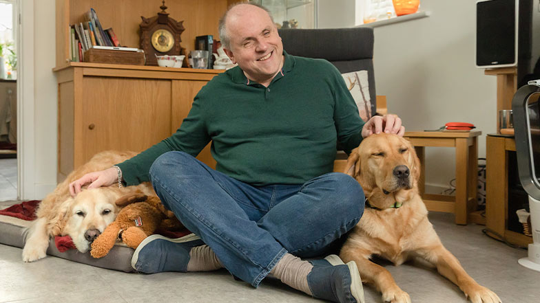 Guide dog owner, John, sits between his retired guide dog and working guide dog.