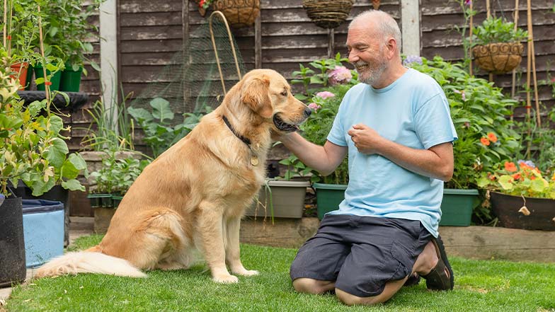 A guide dog owner sits in his garden with his guide dog, as they smile at each other.