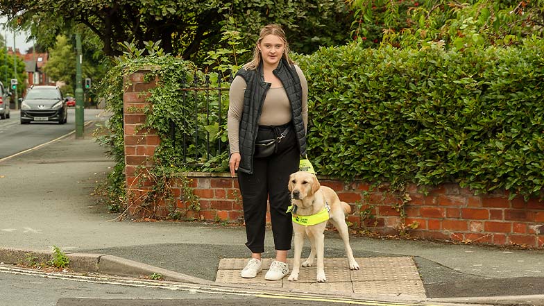 A guide dog owner and her guide dog prepare to cross a road