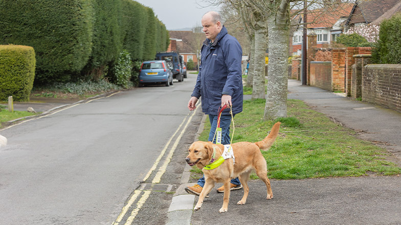 A guide dog owner approaches a drop kerb with his guide dog.