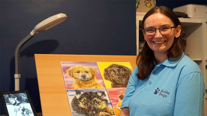 Artist Alex Devlin standing beside a collection of her dog paintings created for Guide Dogs 90th anniversary