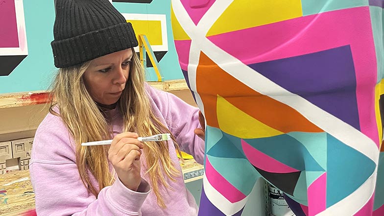 Artist Charlotte from duo Art and Believe painting the guide dog sculpture in a coloured geometric design