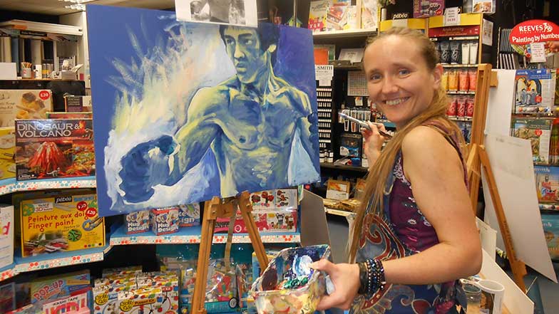 Artist Lois Cordelia in her art studio stood in front of a painting of Bruce Lee