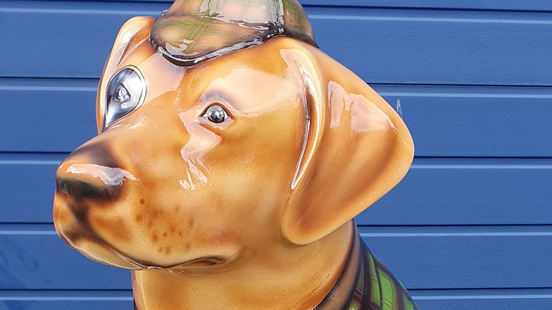 Close-up of a decorated guide dog sculpture head of a realistic looking dog wearing a deerstalker hat.