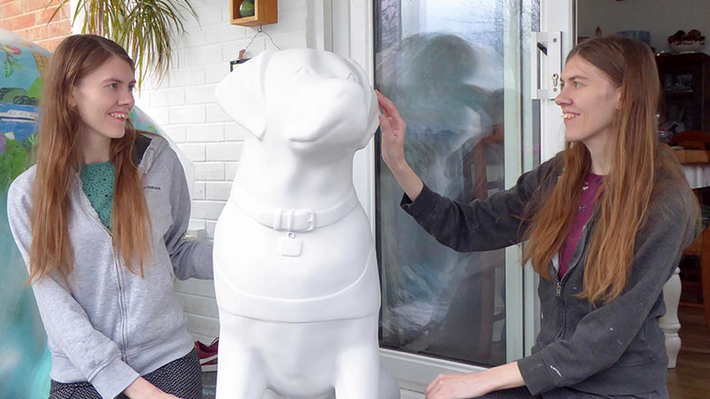 Sisters and artist duo Phillippa and Rachael Corcutt standing beside a blank guide dog sculpture