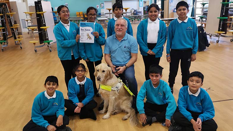 Guide dog owner Dave and guide dog Faldo sat with pupils from Ben Jonson Primary School with their design competition winners certificate