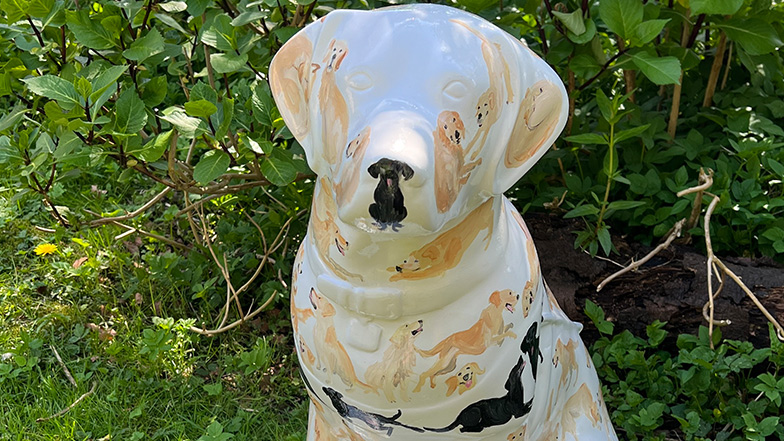 Head and shoulders image of a white mini guide dog sculpture painted with small yellow and black Labradors and golden retrievers.