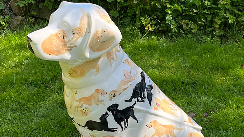 Side top view of a white mini sculpture painted with small yellow and black Labradors and golden retriever dogs.