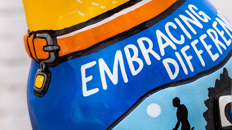 Close up of the side of the sculpture's chest. It has an orange colour and the top of the chest is painted blue with the words 'embracing difference' painted on.