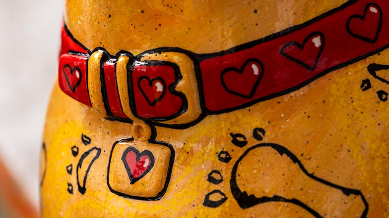 Close up of the sculpture's chest showing a red collar with black hearts and a heart tag. The chest is painted to look like sand and has a black paw and foot print.