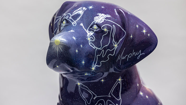 Close up of the sculpture's head which is painted purple with a white dog shaped star constellations painted on each eye and the neck.